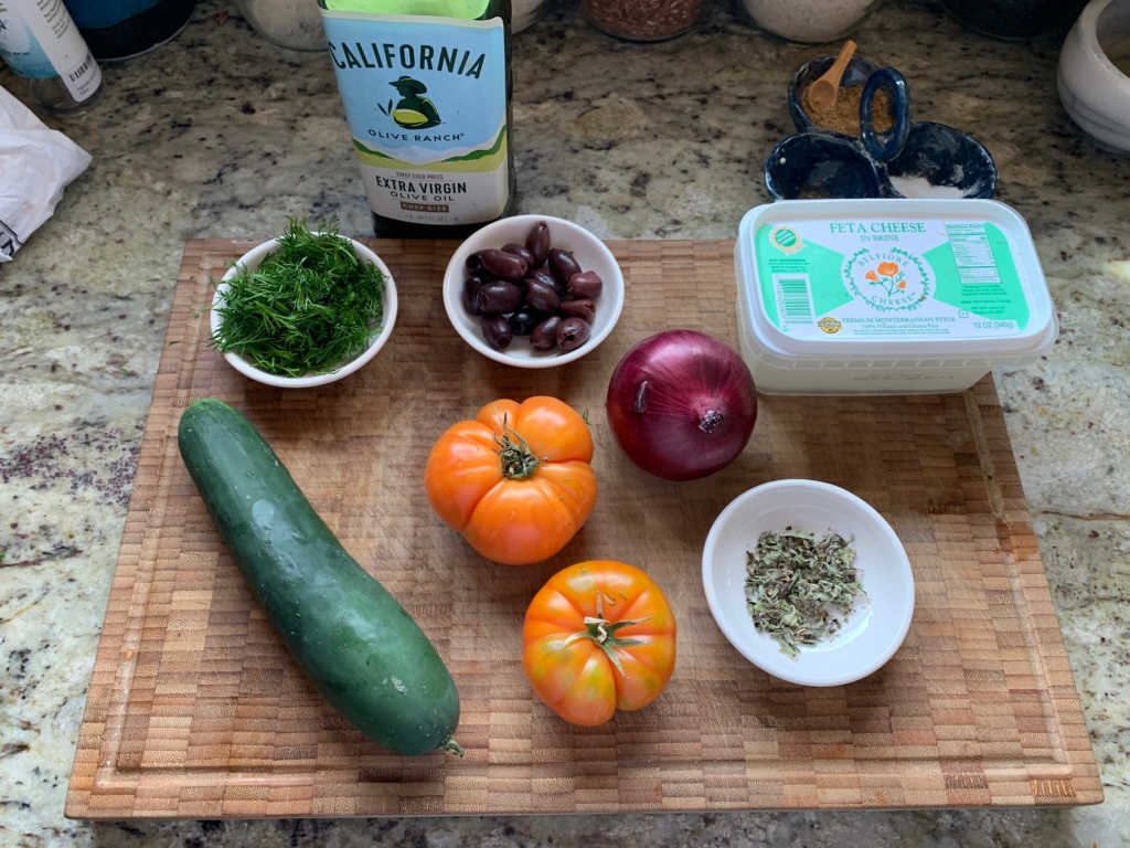 My cutting board with the ingredients: cucumber, tomatoes, onion, olives, deill, olive oil, eta cheese and oregano.