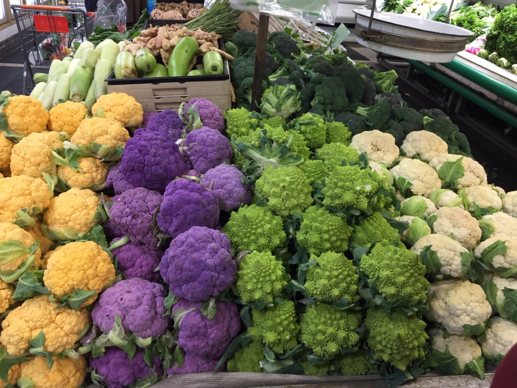 A picture of yellowish orange, purple and white cauliflower with a green remanesco broccoli.