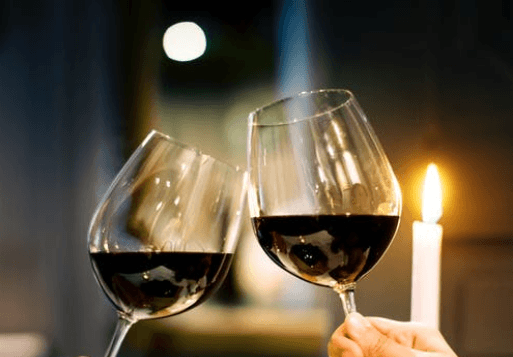 Photo of two wine glasses filled with red wine, clinking.