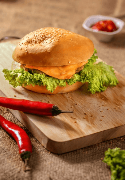 Photo of a burger on a small cutting board with lettuce and red peppers on the side.