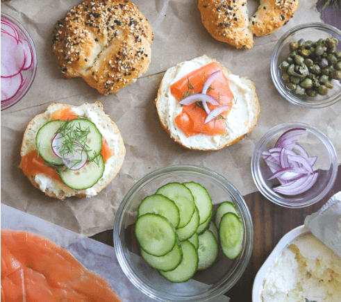 Picture of open bagels with cream cheese, cucumbers, salmon, onions, capers. 