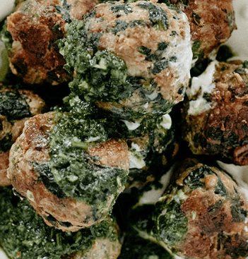 A closeup photo of turkey meatballs with tahini sauce and Chimichurri.