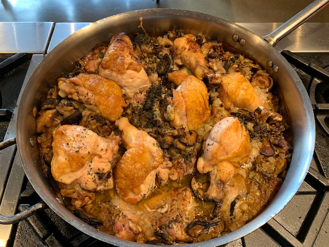 A skillet full of braised chicken thighs with a mushroom sauce.