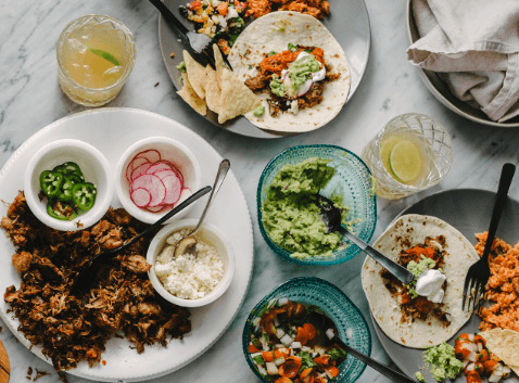 Taco table with tortillas, salad, jalapeño, onions, radishes, and guacamole.