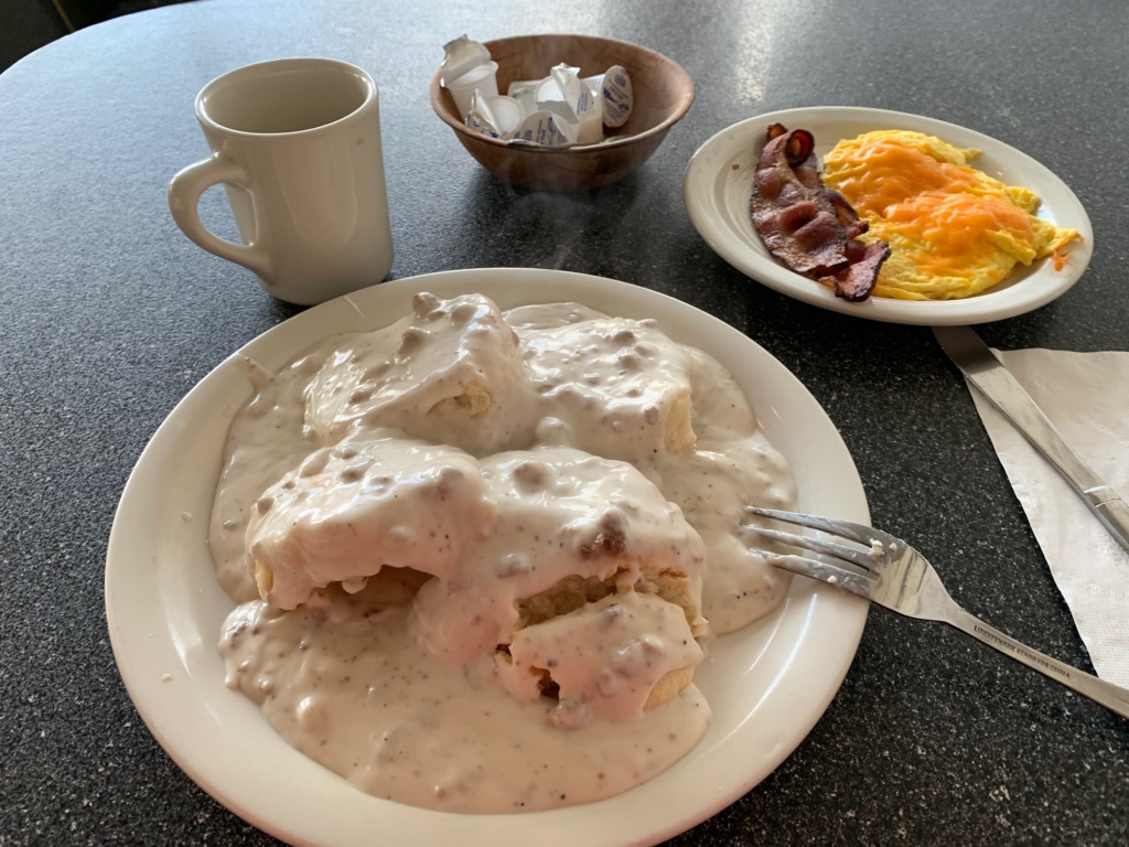 Biscuits and gravy breakfast with a side of scrambled cheese eggs, bacon and coffee.