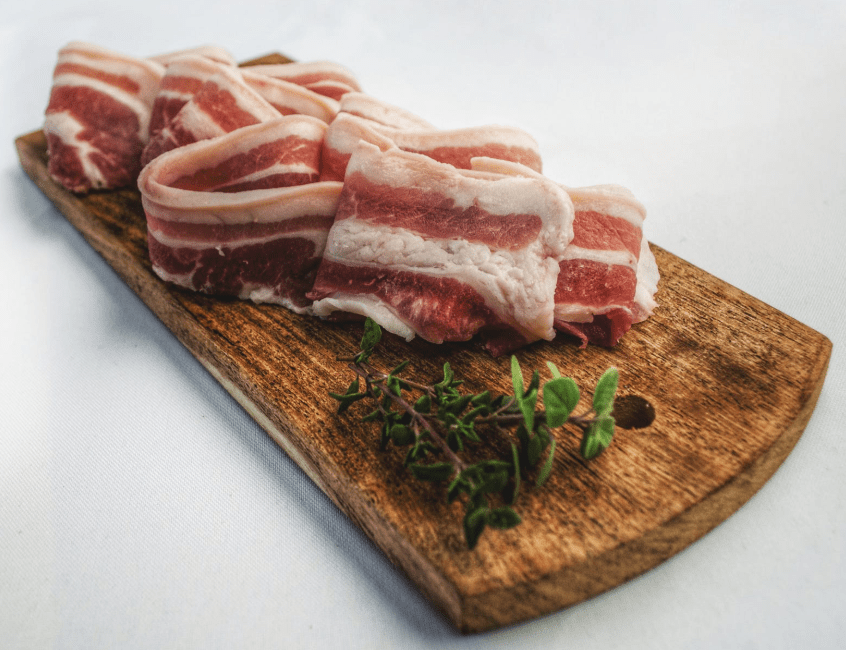 Photo of a few raw bacon slices on a cutting board.