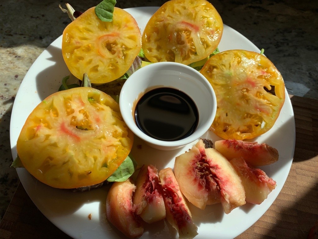 Photo of a California BLT and a side of sliced peaches with a center ramekin with vinegar.