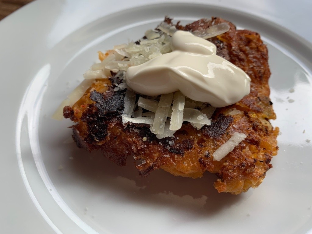 Photo of a fritter with cheese and a dollop of sour cream.