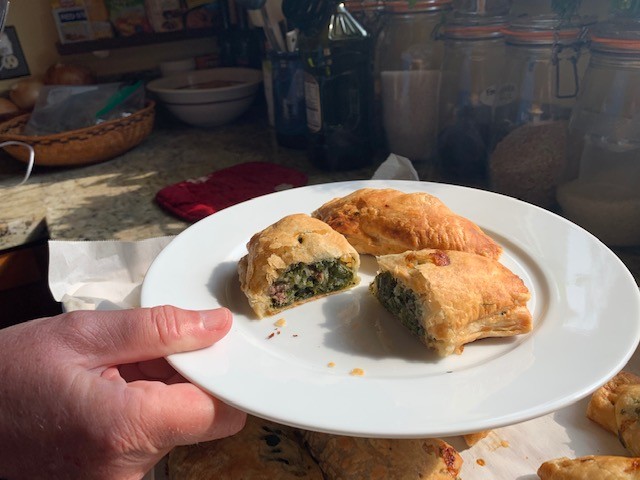 A photo showing two meat pies on a white dish, with one cut open to show the filling.