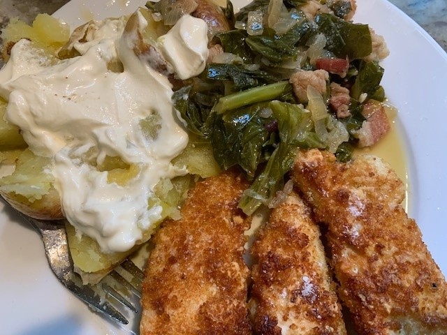 A photo of a Southern dinner of fried chicken, baked potatoes (with butter and sour cream) and collard greens.