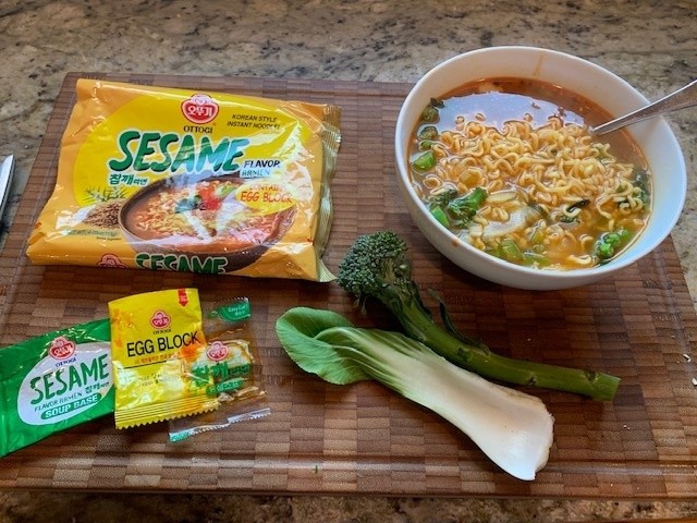 Photo of the package and packets, next to a bowl of soup and a bok choy leaf and sprig of young broccoli.