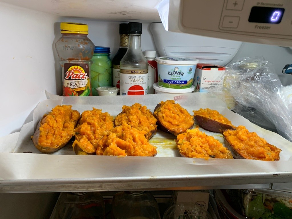 A parchment lined baking dish with the once baked and prepped sweet potatoes sitting on the top shelf of my fridge. Although uncovered for the photo they will be convered.