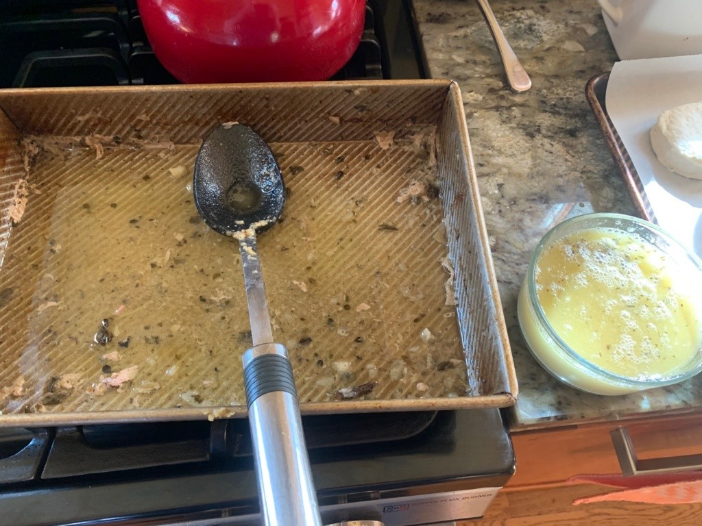 Photo of the turkey baking pan with liquid, meat particles, and herbs ready for making a gravy.