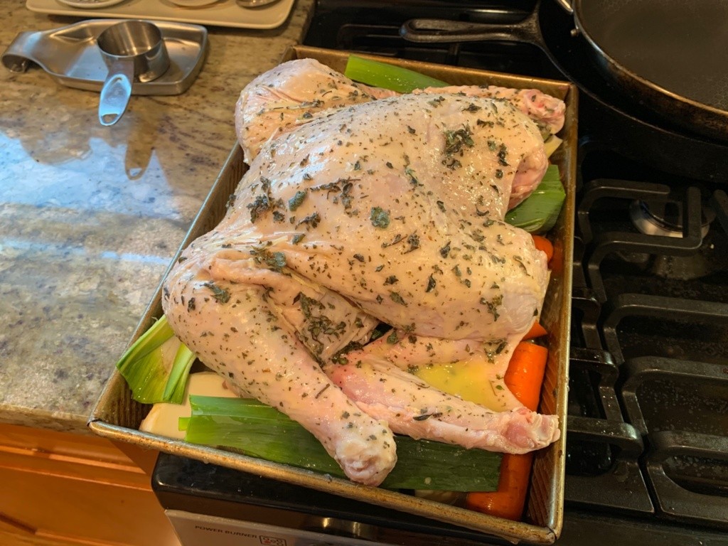 The turkey all covered in butter and herbs, sitting on freshly cut veggies of green, orange, and white, sitting in the baking pan.