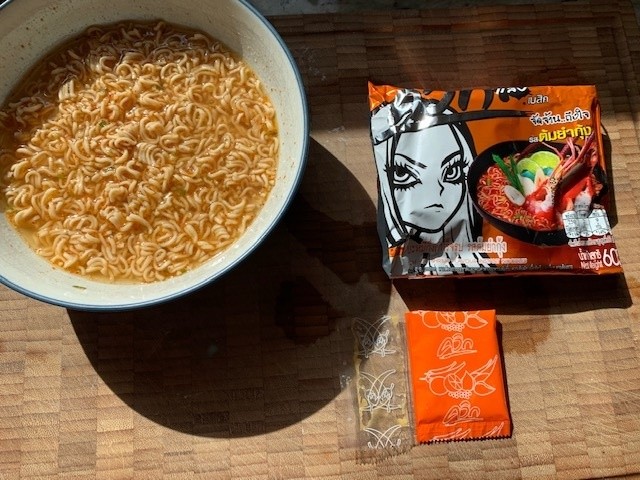 A white ceramic bowl of noodles with packaging.