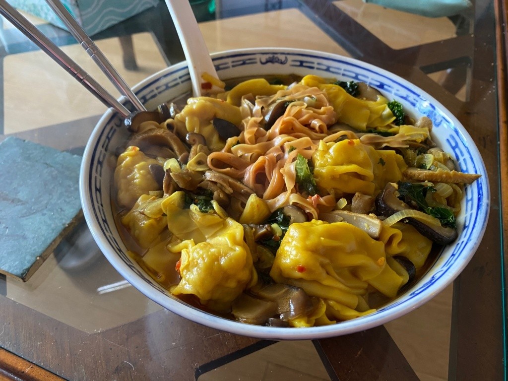 A ceramic bowl of beutiful soup with noodles, dumplings and veggies.