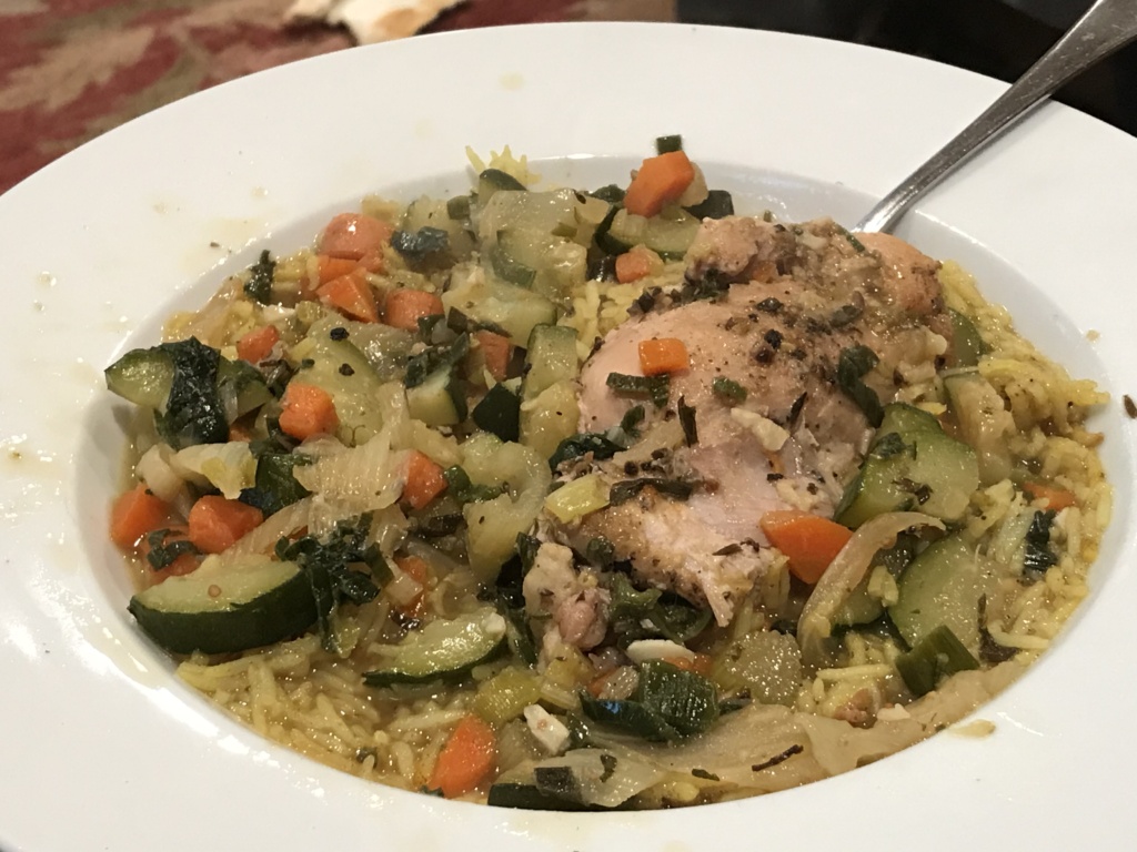 Photo of a white low bowl with rice, broth, veggies and a chicken thigh.