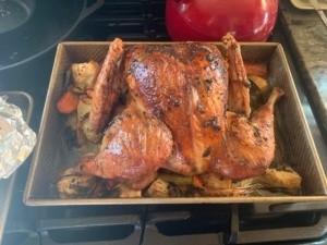 The browned, cook turkey in its baking pan with some of the cooked veggies showing. I am about to remove the turkey from the pan to rest.