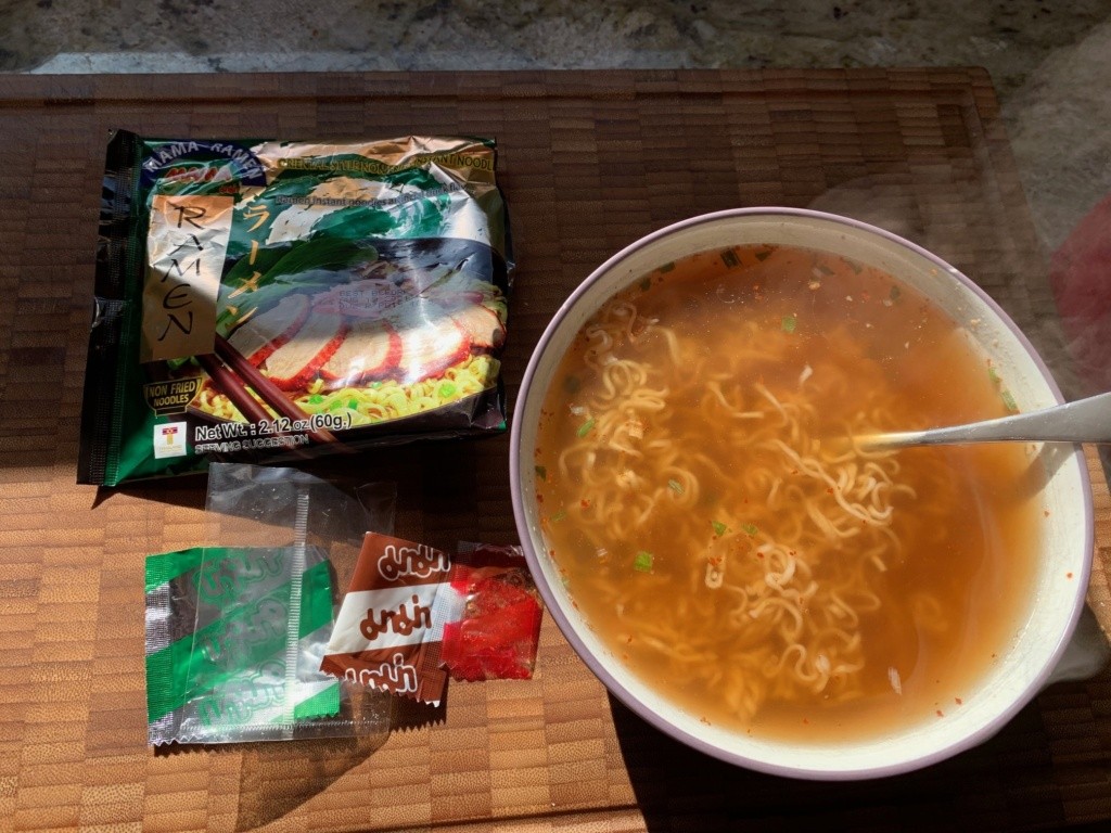 Photo of the packaging and a reddish noodle soup with flecks of scallions.