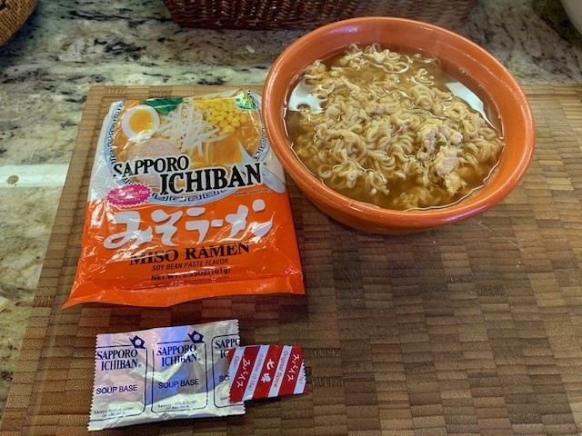 Photo of an orange colored bowl of ramen + egg, and the soup pacakages.