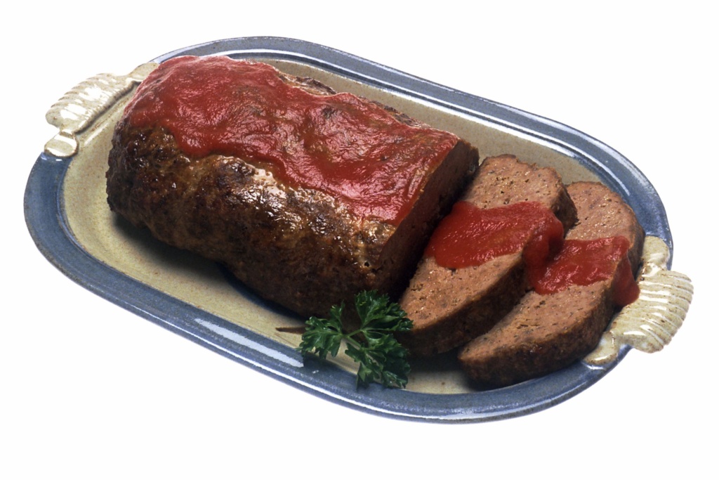 A photo of a ketchup covered loaf of meatloaf with a couple of cut slices.