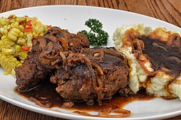 A plate of salisbury steak with mashed potatoes and gracy and a side of mixed veggies.