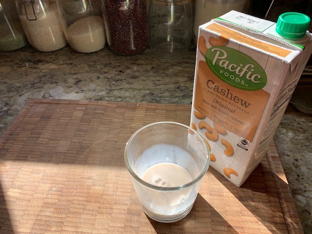 A picture of a glass of cashew milk and its container.