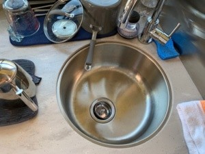 A picture looking down on the round, stainless steel kitchen sink. Also showing is dishes drying on a dish towel, and my tea kettle.