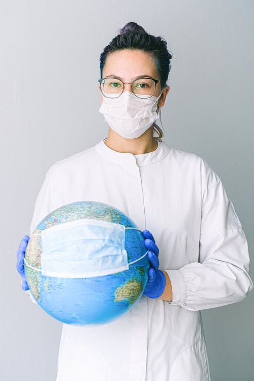 Masked woman in gloves holding an earth globe that is also masked.