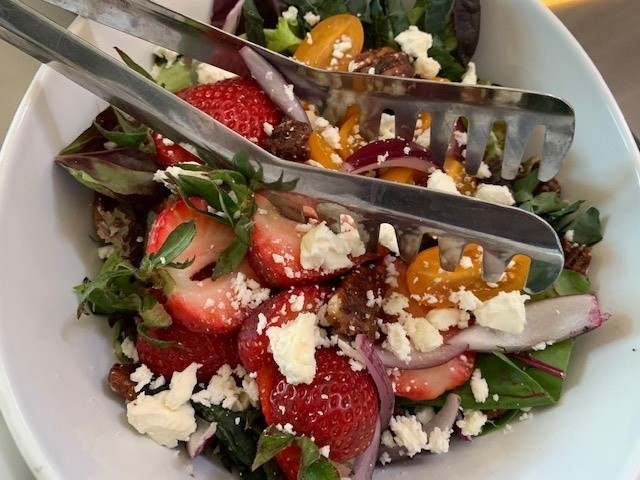 This salad is served in a white bowl and the colors are vibrant greens, yellow form the tomatoes, and brilliant red from the strawberries.