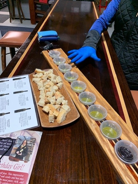 The layout of our olive oil tasting adventure. A plank with plastic containers of around 1T of oil from each variety. Plus a platter of torn up bread for dipping. A sheet with descriptions nearby.