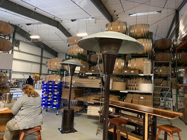 A picture to my right while sitting in the storage facility. Tasting tables are distantly placed, the space is large and mainly filled with storage barrels.